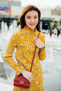 Portrait of smiling woman holding yellow while standing outdoors