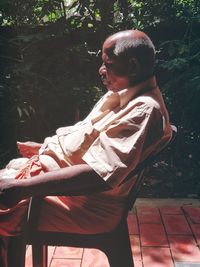 Side view of young man sitting on seat against trees
