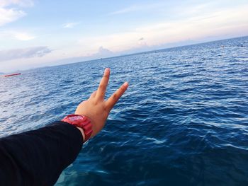 Cropped hand gesturing peace sign against sea