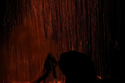 Rear view of silhouette woman standing against illuminated lights at night