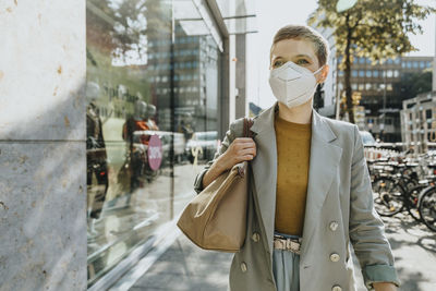 Woman wearing protective face mask walking on street during sunny day