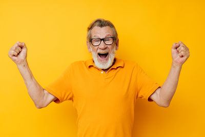 Senior man gesturing against yellow background