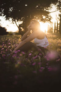 Boring teenager sitting in the field among flowers at sunset