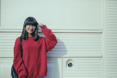 Asian teenager wearing red sweater standing against white wall