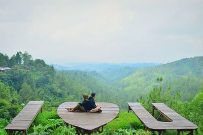 Rear view of man and women sitting on mountain against sky