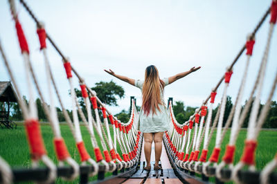 Rear view of woman with arms raised standing against sky