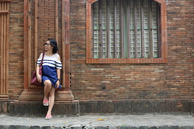 Young woman carrying purse while standing on footpath against building