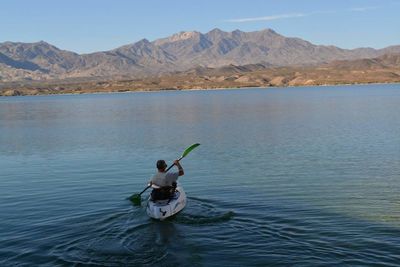 Rear view of man kayaking in lake against mountains