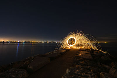 Man standing amidst illuminated wire wool by sea at night