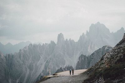 Distant view of men hiking on mountains against sky