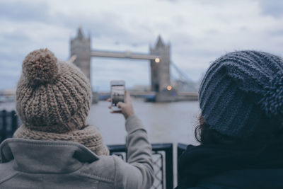 Rear view of woman with friend photographing london bridge