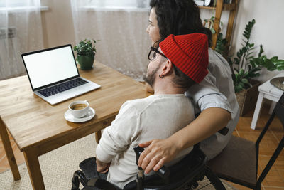 Woman sitting by boyfriend with disability looking at laptop on table