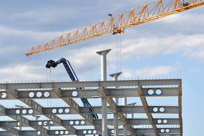 Low angle view of crane at construction site against sky