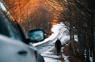 Front view of person walking on snow covered forest road at sunset