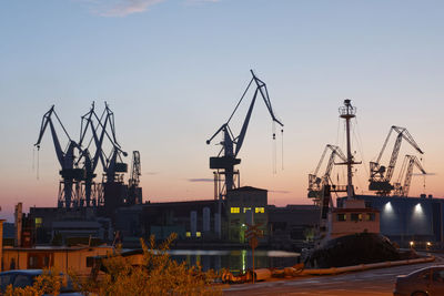 Cranes at construction site against sky during sunset