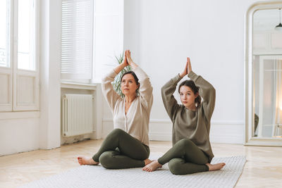 Attractive mother middle age woman and daughter teenager ptactice yoga together in bright room