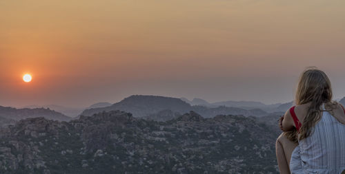 Rear view of person standing on landscape against sky during sunset