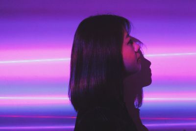 Portrait of young woman looking away while standing against wall