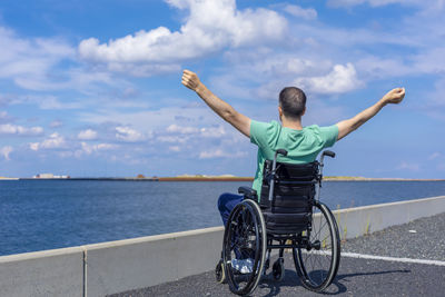 Rear view of man sitting by sea against sky