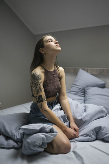 Woman with tattoo sitting on the bed.