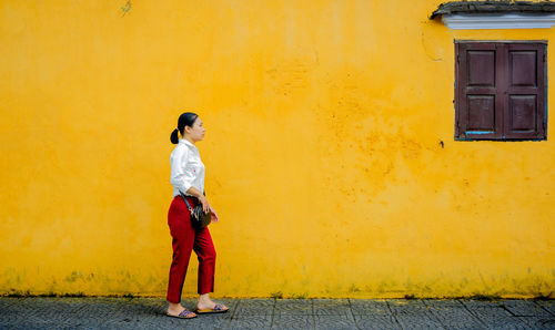 Side view of young woman standing on road against wall