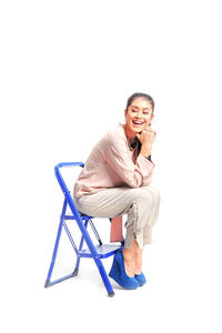 Smiling fashionable woman sitting on ladder against white background