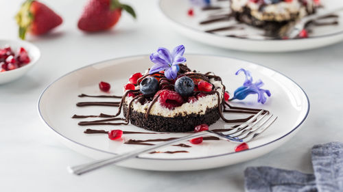 Close up of a mixed berry cheesecake drizzled with chocolate, ready for eating.