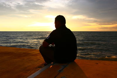 Silhouette man sitting on beach against sky during sunset