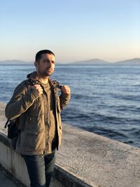 Man standing at sea against clear sky during sunset