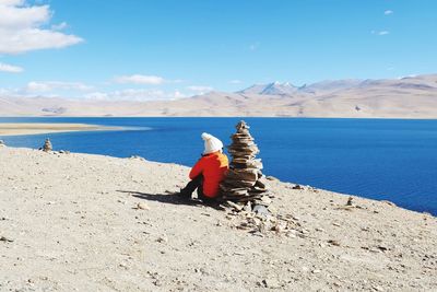 Rear view of woman sitting by stacked stones at beach