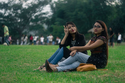 Portrait of friends sitting on field against sky