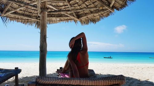 Woman resting on bed below thatched roof parasol at beach