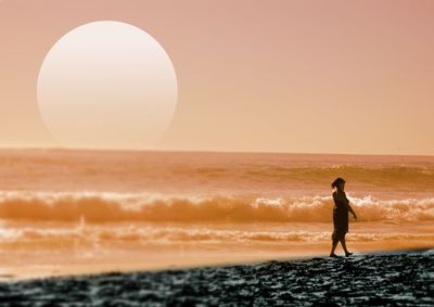 Woman walking at beach against sky during sunset