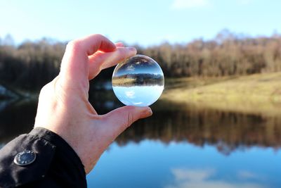 Close-up of hand holding crystal ball against calm lake