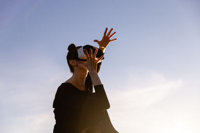 Low angle view of woman with arms raised standing against clear sky