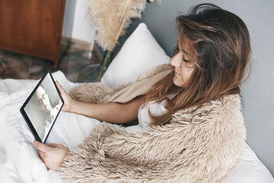 High angle view of woman using digital tablet while sitting on bed