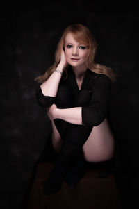 Portrait of young woman sitting against black background