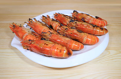 Plate of flaming grilled river prawns served on wooden table