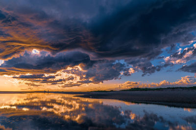 Scenic view of lake against dramatic sky during sunset