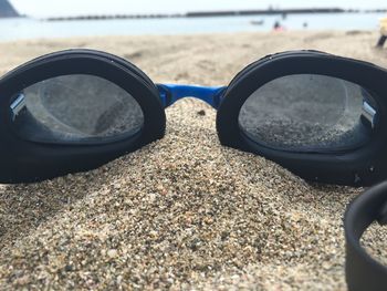 Close-up of swimming goggles on sand at beach