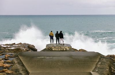 People standing on rock by sea against sky