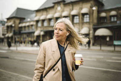 Businesswoman looking away while holding disposable coffee cup in city