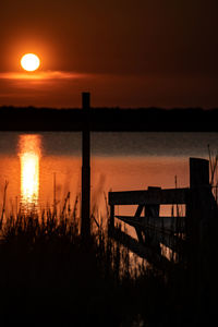 Silhouette railing by lake against sky during sunset