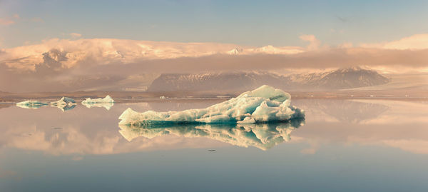 Panoramic view of frozen lake against mountains at sunset during winter