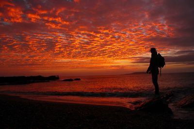 Silhouette woman standing on beach against orange sky