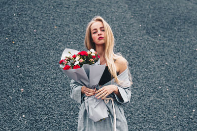 Portrait of beautiful woman holding bouquet standing against wall
