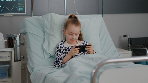 Girl playing video game relaxing on bed at hospital