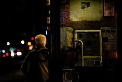 Rear view of man standing on illuminated street