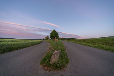 Empty road amidst field against sky