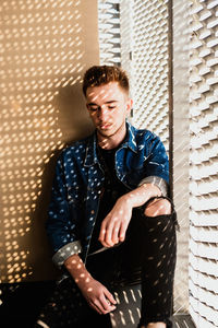 Young man looking away while standing against wall